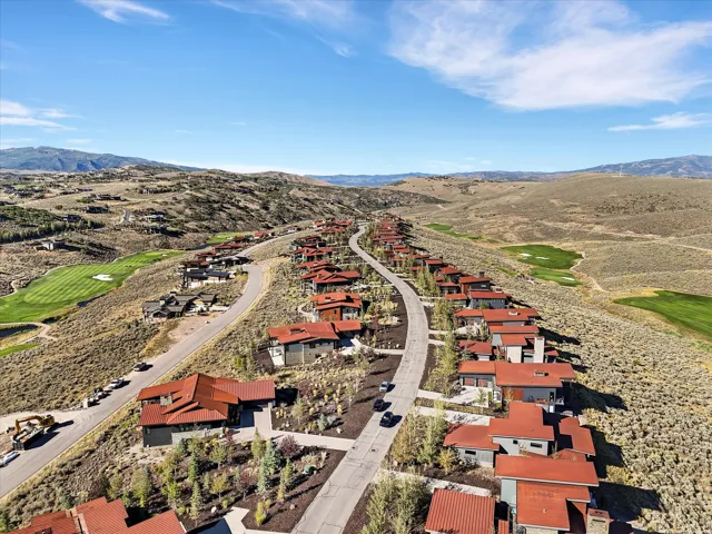Modern residential development featuring a paved road, integrated landscaping, and distant golf course access