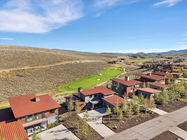 Contemporary architecture with red metal roofing, an expansive drive, and mature landscaping