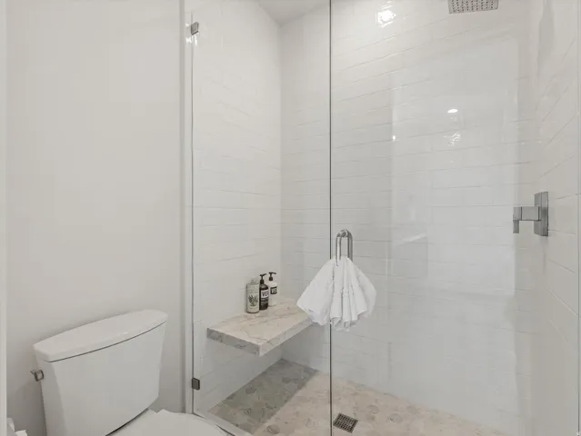 Glass-enclosed shower with subway tile surround, rain shower head, built-in marble-finish bench, and pebble-finish floor