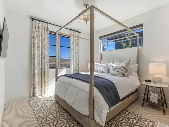 Recessed lighting, wood-finish four-poster bed frame, two permanent wall-mounted windows, and light-toned carpet
