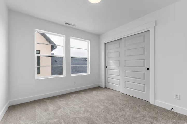 Carpeted flooring, white walls, dual windows, and a built-in closet with paneled doors