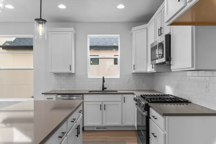 White cabinetry with dark hardware, subway tile backsplash, stainless steel appliances, and a gas range