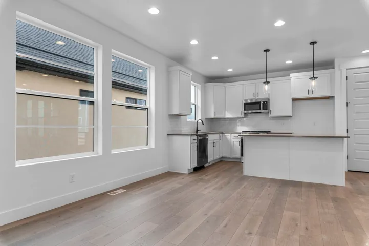 Open-concept kitchen featuring white cabinetry, stainless steel appliances, a center island with seating, and pendant lighting