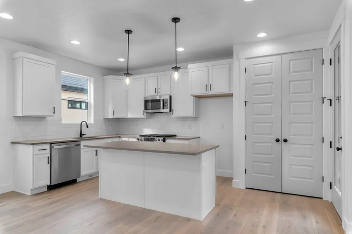 Kitchen featuring white shaker cabinetry, stainless steel appliances, a center island with countertop, recessed lighting, and wood-finish flooring