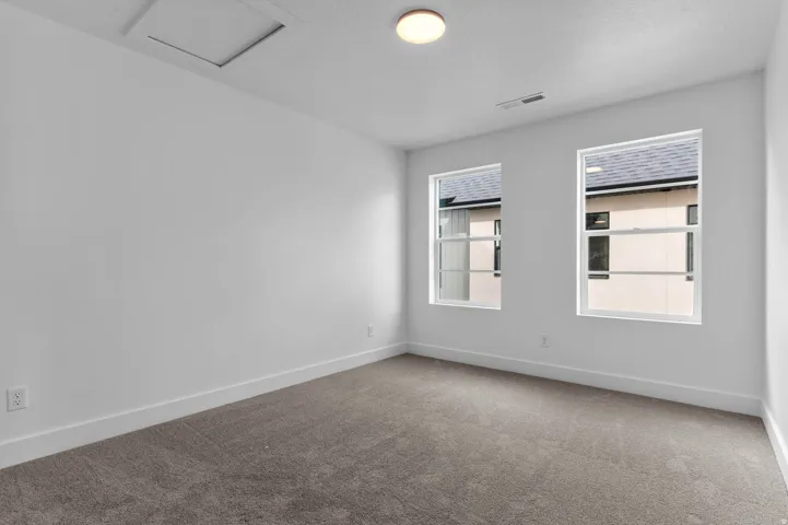 Neutral wall paint, carpet flooring, two double-hung windows, and a flush mount ceiling light