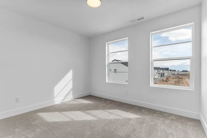 Two large windows, plush carpet flooring, white walls, and a flush mount ceiling light