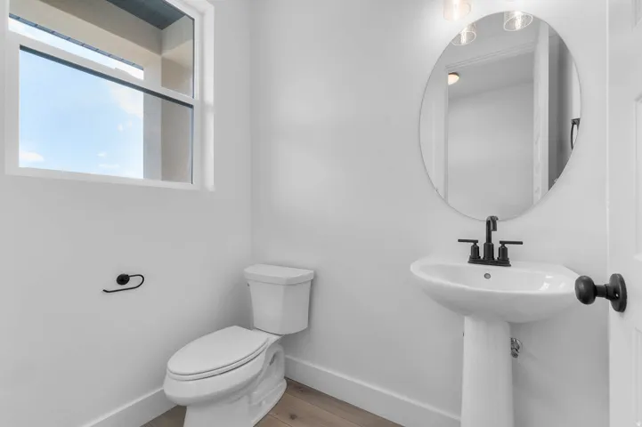 White pedestal sink with matte black faucet, oval mirror, and wood-finish flooring