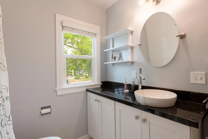 White vanity with crystal knobs, dark countertop, vessel sink, and wall-mounted faucet