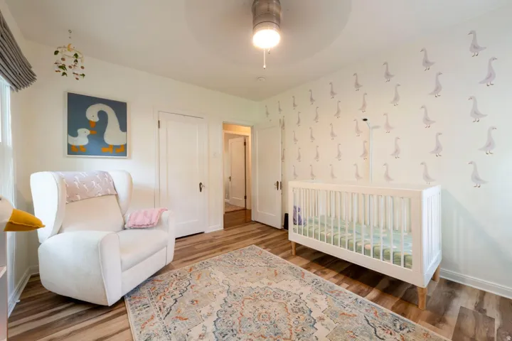 White walls with decorative accents, wood-finish flooring, a white door, and a ceiling fan with integrated lighting