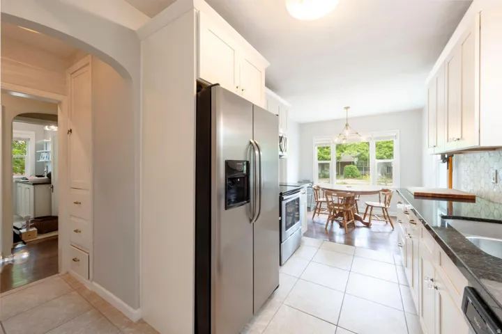 Galley kitchen featuring stainless steel appliances, white cabinetry, dark countertops, and tile flooring