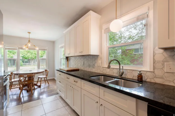 White shaker-style cabinetry with dark hardware, black countertops, and a hexagonal tile backsplash