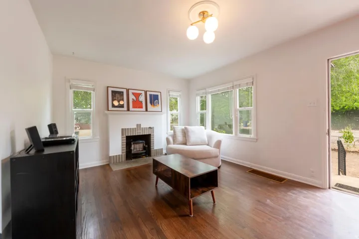 Living area featuring wood-finish flooring, a white brick fireplace with a hearth, multiple windows, and a contemporary ceiling light fixture