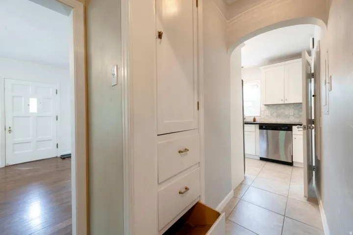 Built-in white cabinetry, tiled flooring, arched doorway, white paneled door, and wood-finish flooring