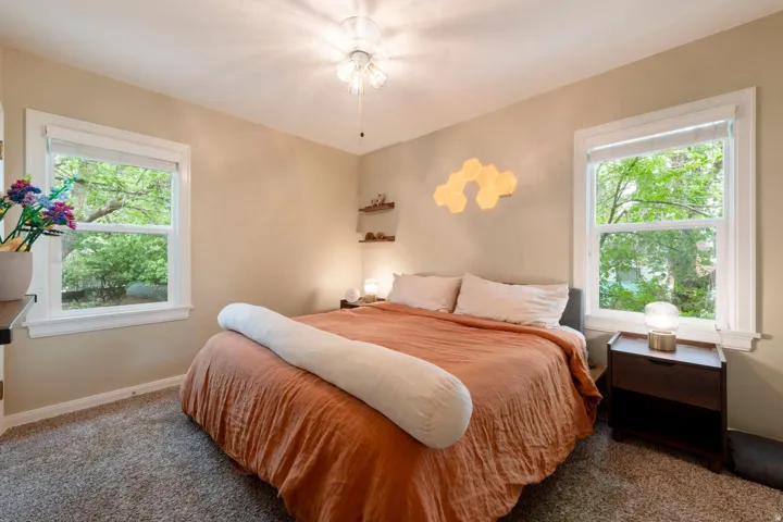 Soft neutral wall color, two windows with white trim, ceiling fan, and carpeted flooring