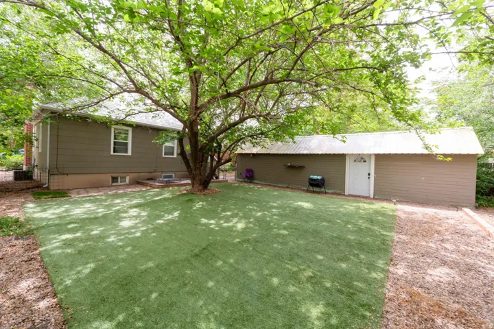 Expansive backyard featuring artificial turf, mature tree, and a detached structure with a metal roof