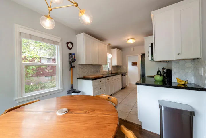 White shaker cabinetry, black countertops, hexagonal tile backsplash, tile flooring, and a modern ceiling light fixture