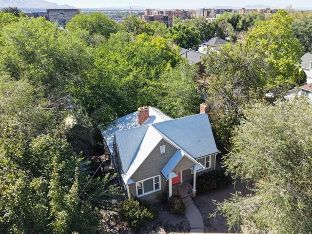 Gabled roofline, brick chimney, covered entry, and mature perimeter trees