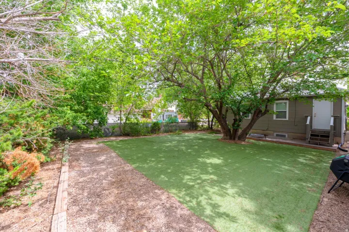 Expansive backyard featuring artificial turf, mature tree, gravel pathway, and a chain-link fence