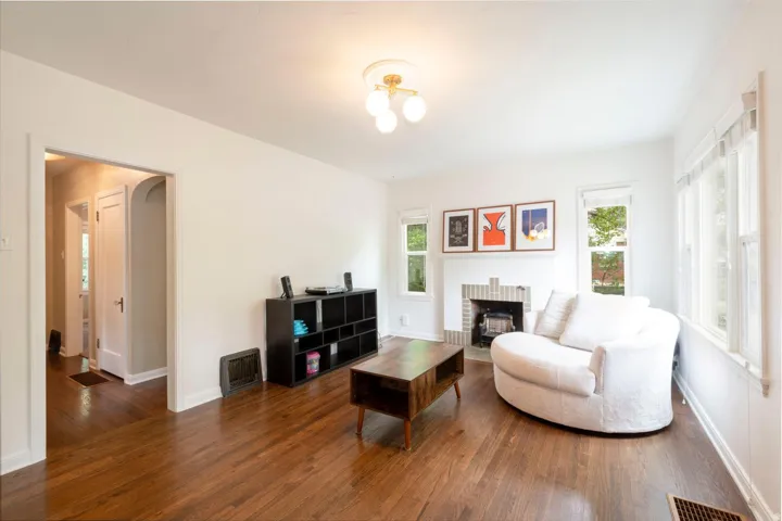 Hardwood flooring, white walls, decorative fireplace with brick surround, recessed windows, and flush-mount ceiling light fixture
