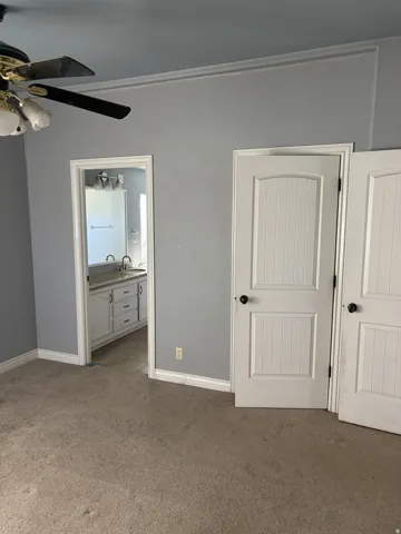 Ceiling fan with light fixture, carpeted flooring, two paneled doors, and a bathroom vanity with dual sinks