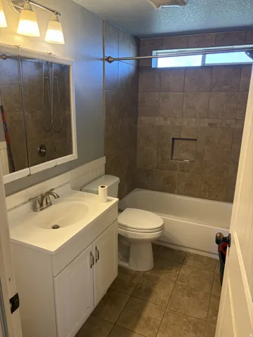 Tile flooring, white vanity with integrated sink, tiled bath surround with decorative accent band, built-in shower niche, and high window