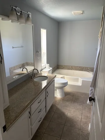Dual vanity with undermount sinks and light-toned countertop, tile flooring, built-in bathtub, and recessed window