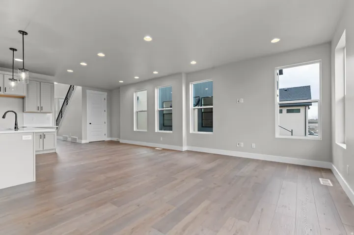 Spacious interior with wood-finish flooring, recessed lighting, multiple windows, and a kitchen island with pendant lighting and a gooseneck faucet