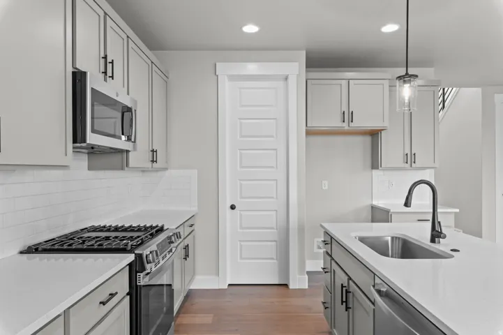 Kitchen featuring light gray cabinetry, stainless steel appliances, white subway tile backsplash, white countertops, and wood-finish flooring