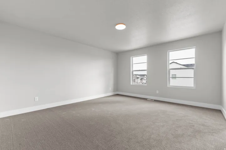 Spacious room featuring neutral carpeting, light-toned walls, and multiple windows
