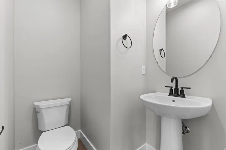 Pedestal sink with matte black faucet, wall-mounted oval mirror, and white toilet