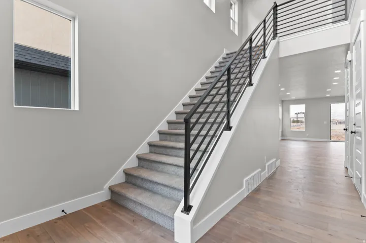 Wood-finish flooring, carpeted staircase with metal railings, recessed lighting, and white paneled doors