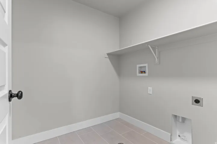Laundry area featuring a built-in shelf, neutral wall tones, and light-toned tile flooring