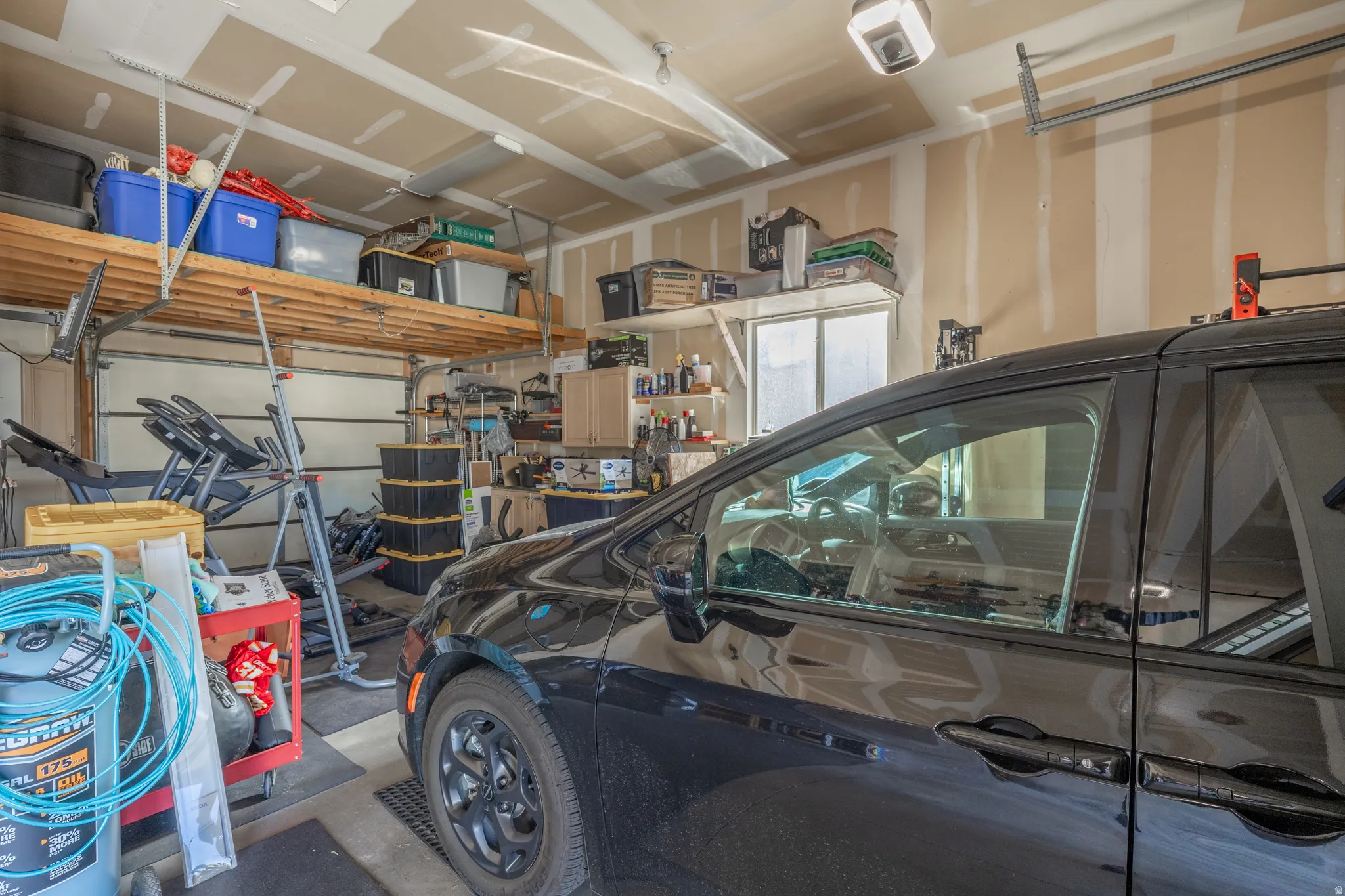 Extra-deep garage bay featuring an EV charging hookup, pull-through rear garage door, overhead storage, and installed workout equipment—offering exceptional flexibility for vehicles, recreation, and additional storage.