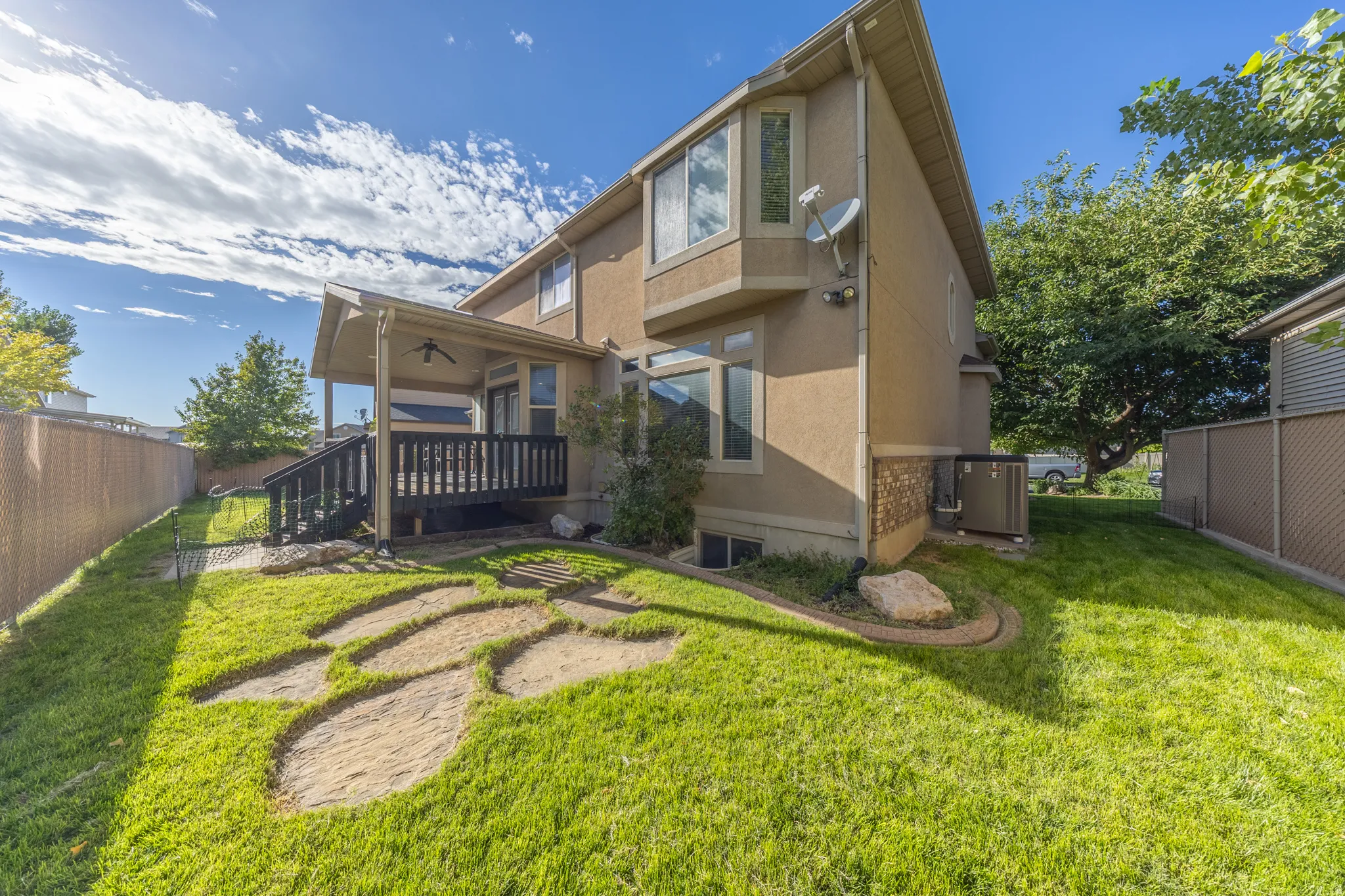 Inviting backyard featuring mature landscaping, a spacious lawn, charming stone pathways, and a covered deck—perfect for outdoor dining, relaxing, and entertaining.