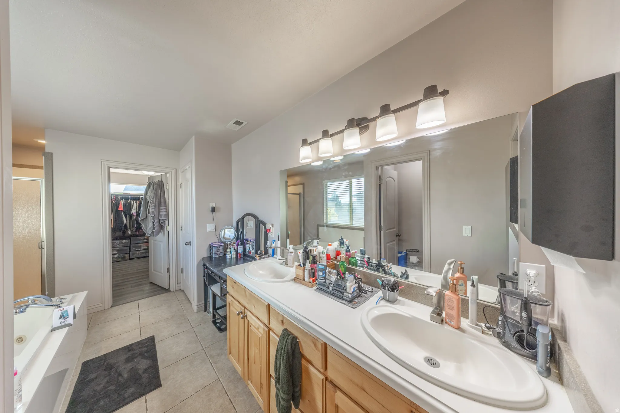 Spacious primary bathroom featuring an expansive dual-sink vanity, relaxing jetted tub, and direct access to a generously sized walk-in closet.