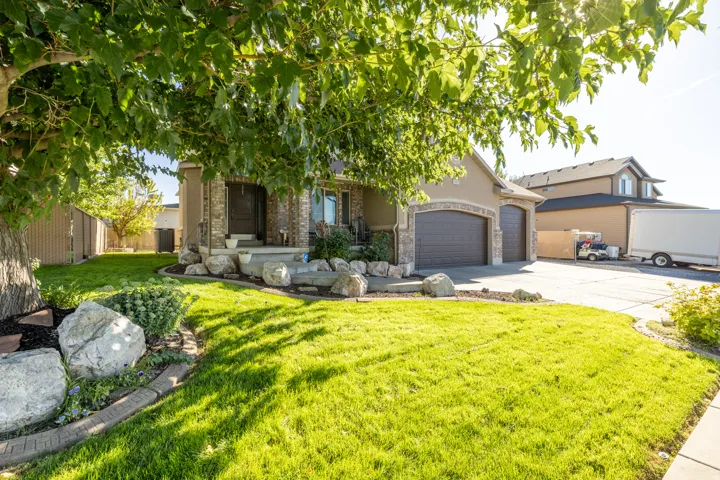Beautiful stucco-and-brick exterior featuring an oversized three-car garage, spacious concrete driveway, dedicated RV/gravel parking, a welcoming covered front porch, mature shade trees, and beautifully maintained landscaping.