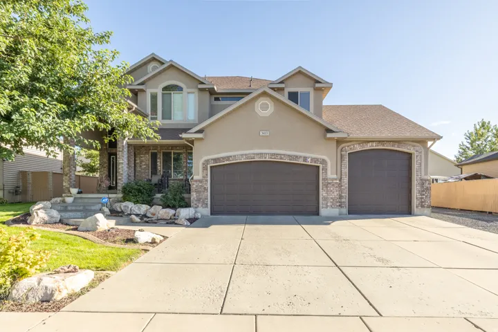 Well-maintained stucco exterior with attractive stone accents, arched garage doors, a spacious concrete driveway, covered front porch with stone columns, and established mature landscaping.