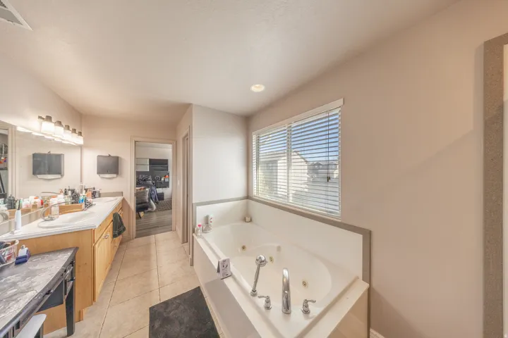 Bright and spacious primary bathroom featuring a relaxing jetted tub beneath a large window, an expansive dual-sink vanity, and direct access to the primary suite