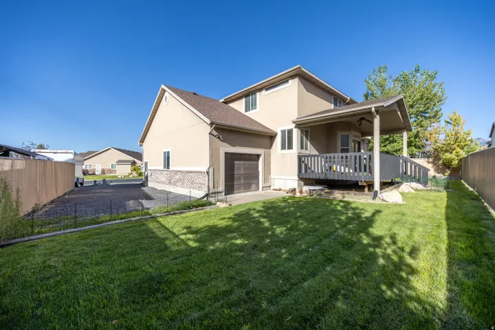 Spacious backyard featuring a lush lawn, covered deck, expansive RV parking, and a convenient rear pull-through garage door—ideal for outdoor living, entertaining, and easy access to recreational vehicles and equipment.