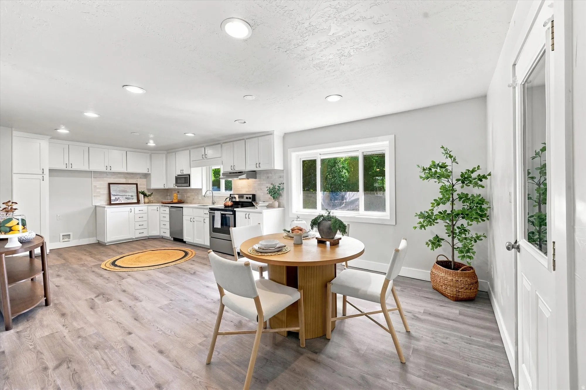 Open-concept kitchen and dining area featuring white cabinetry, stainless steel appliances, wood-finish flooring, and recessed lighting