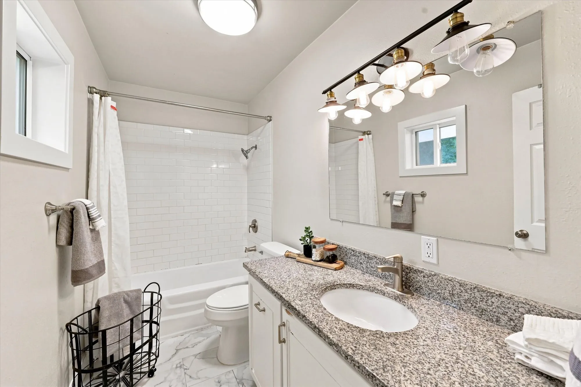 Bathroom featuring a white subway tile shower surround, a built-in bathtub, a window, a single vanity with a stone countertop, and a mirror with a multi-bulb light fixture