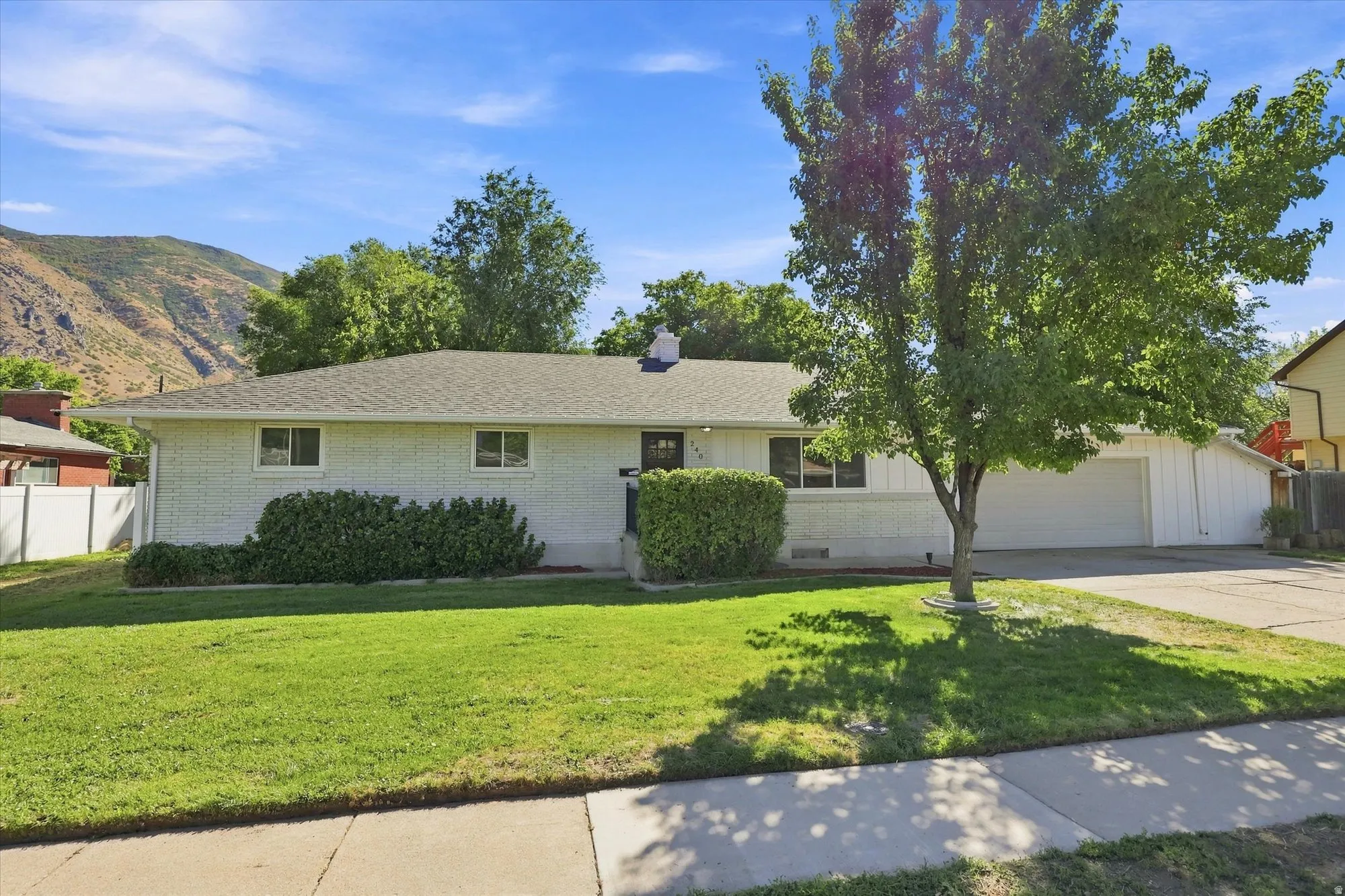 White brick exterior with a dark-shingle roof, attached garage, and a lush lawn