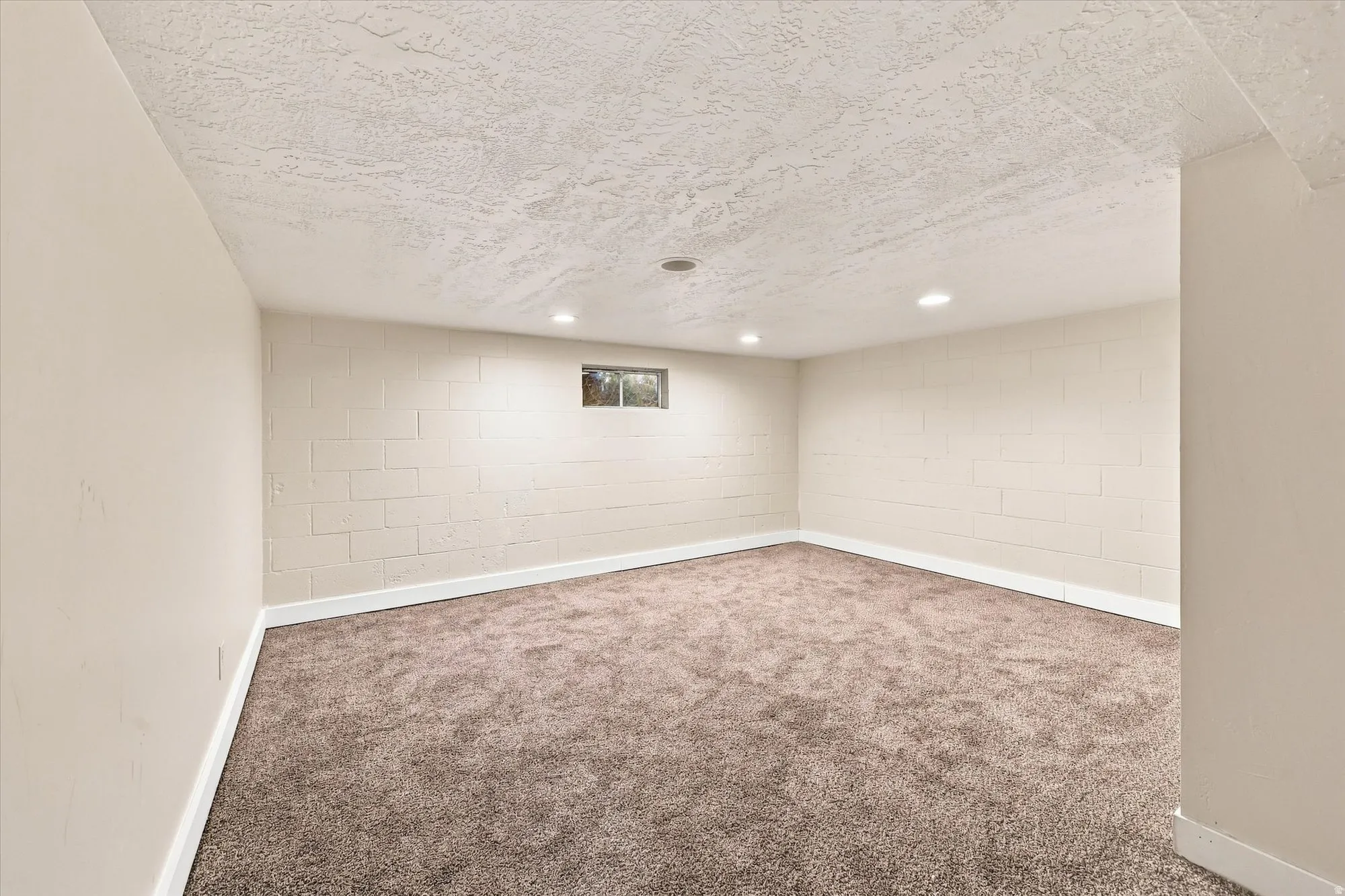 Carpeted room with recessed ceiling lighting, a window, and painted block walls