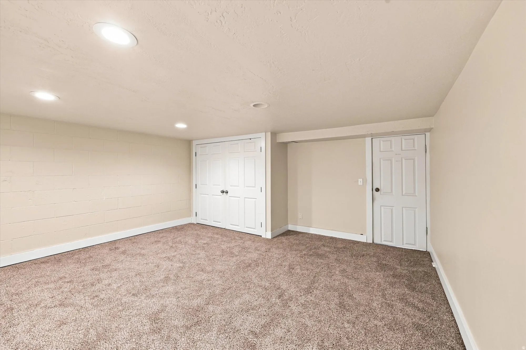 Recessed lighting illuminates the carpeted flooring and light-toned walls