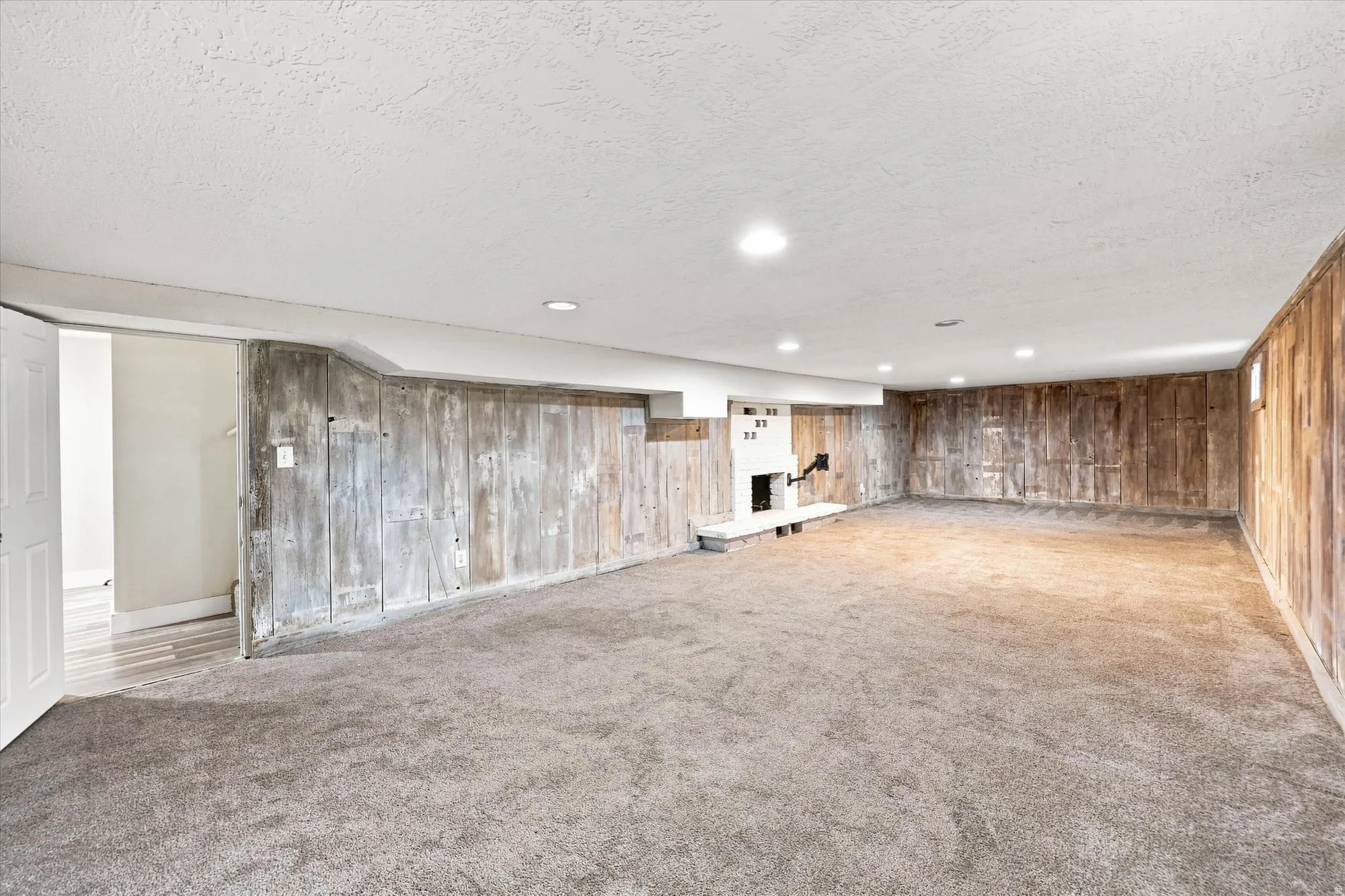 Expansive carpeted area featuring a white fireplace, recessed ceiling lighting, and wood-paneled walls