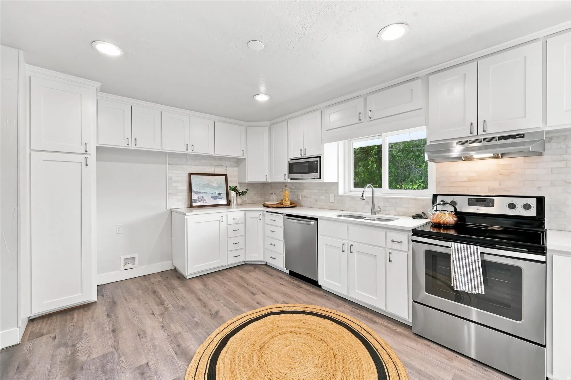 White cabinetry with brushed nickel hardware, stainless steel appliances, wood-finish flooring, recessed lighting, and a subway tile backsplash