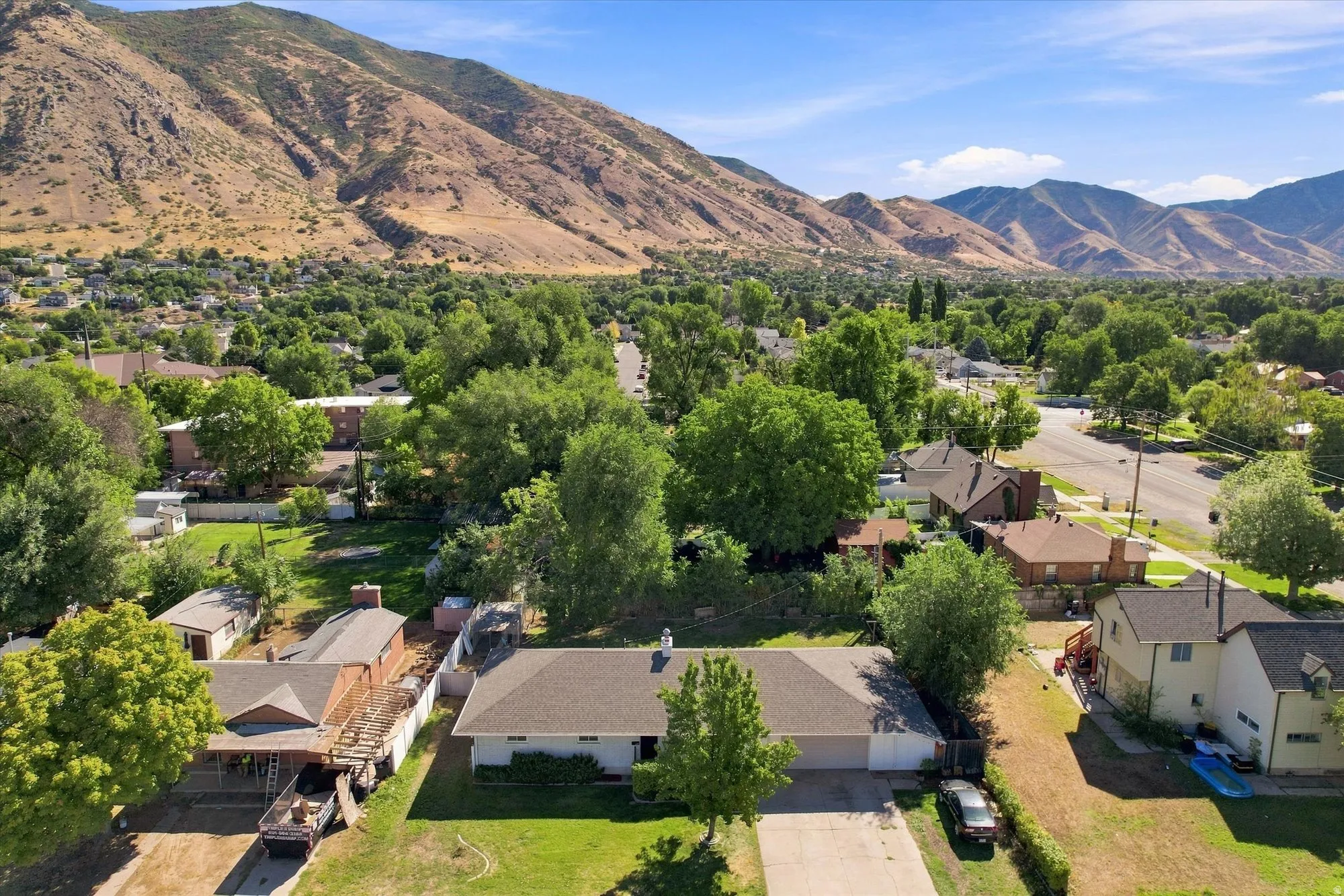 Single-story residence with an attached garage, featuring a paved driveway, mature trees, and a surrounding mountainous landscape