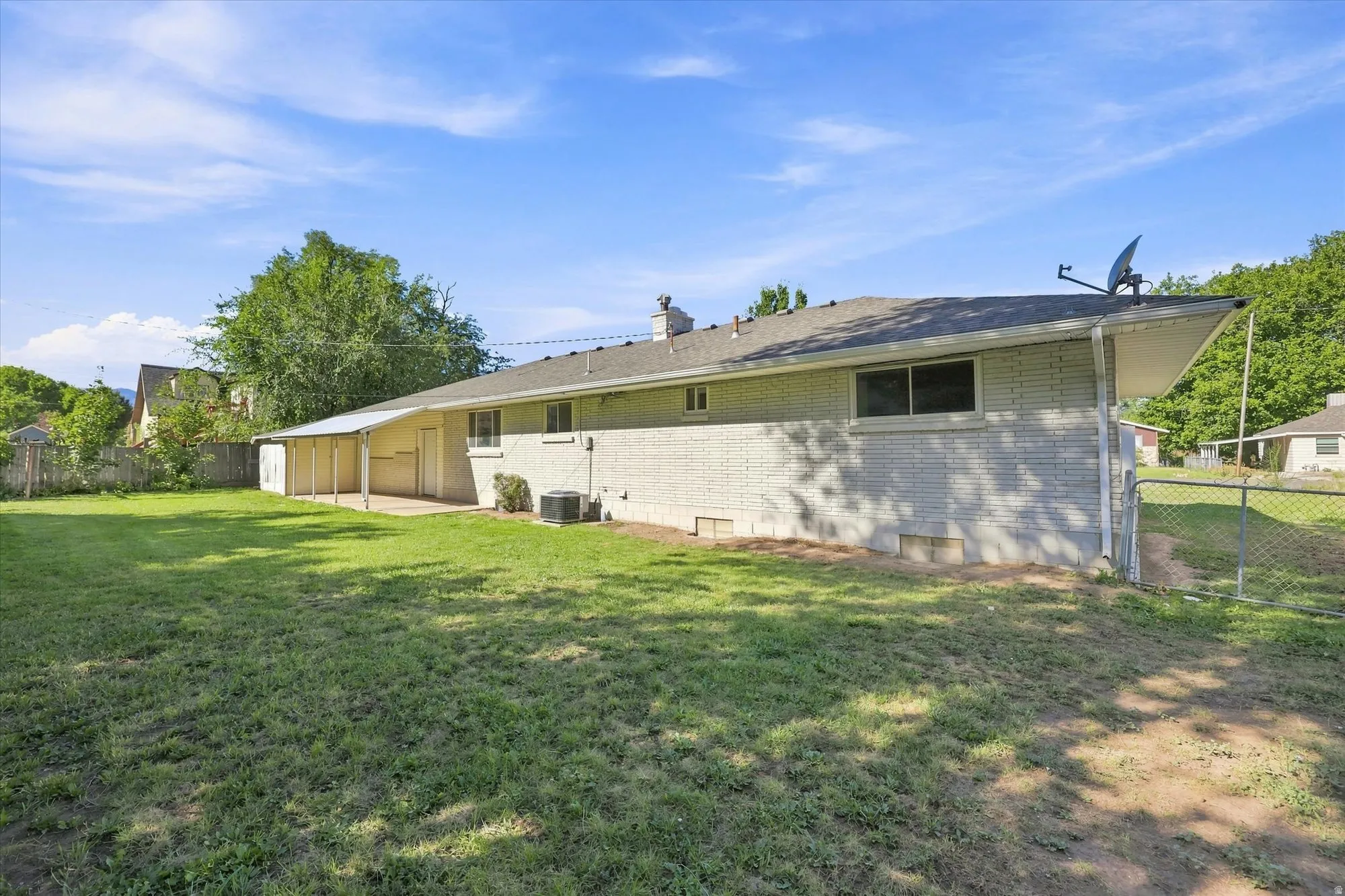 Expansive backyard featuring a manicured lawn, a covered patio, and a chain-link fence
