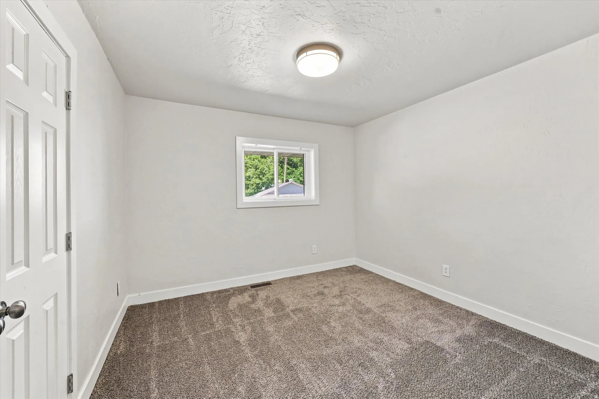 Neutral-toned carpeting, white walls, and a single window with white trim