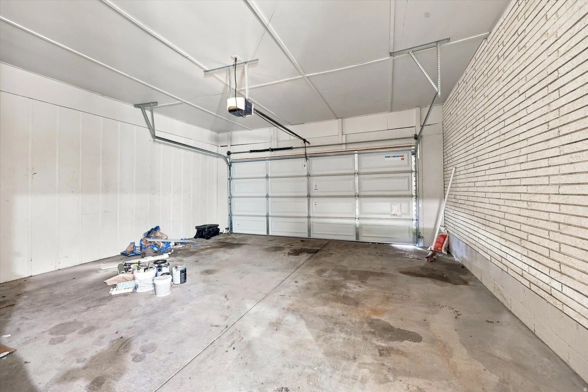 Two-car garage featuring a sectional overhead door, exposed ceiling joists, and a brick accent wall
